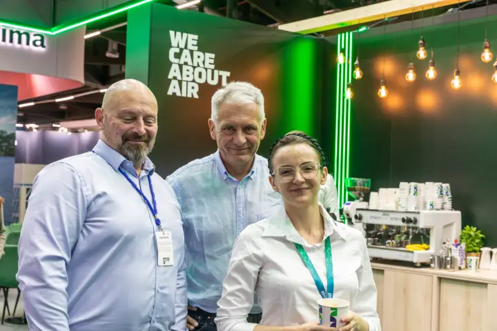 Three visitors at the Klima-Therm café with the "We Care About Air" wall behind at Chillventa 2026