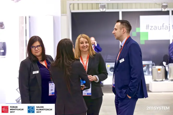 Exhibitor staff chatting in the aisle beside a white stand