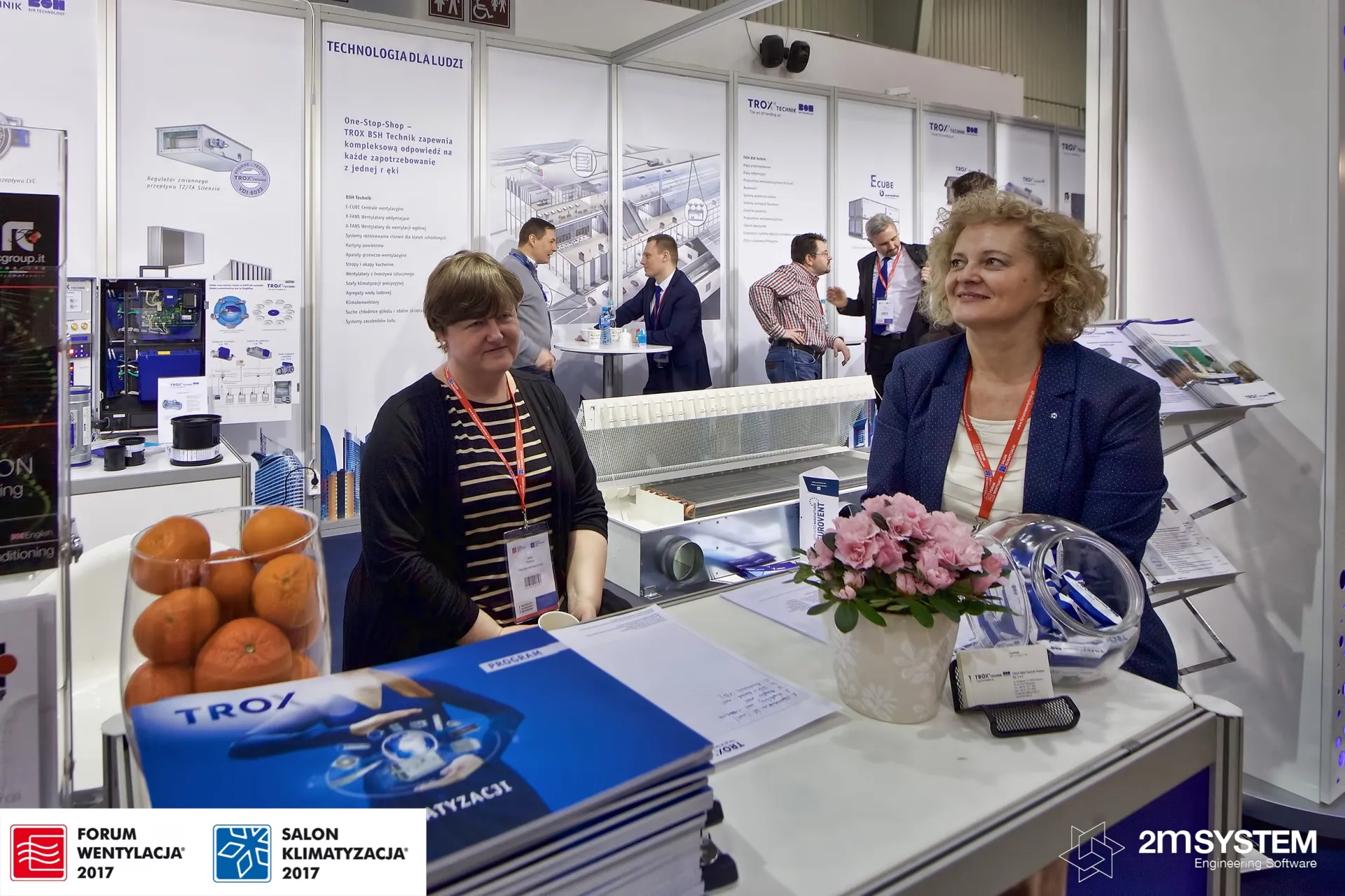 Staff at the Trox Technik reception counter with catalogues and oranges at Forum Wentylacja 2017