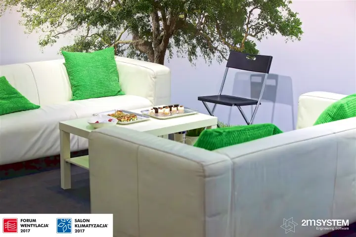 Stand lounge with white sofas, green cushions and a tree mural