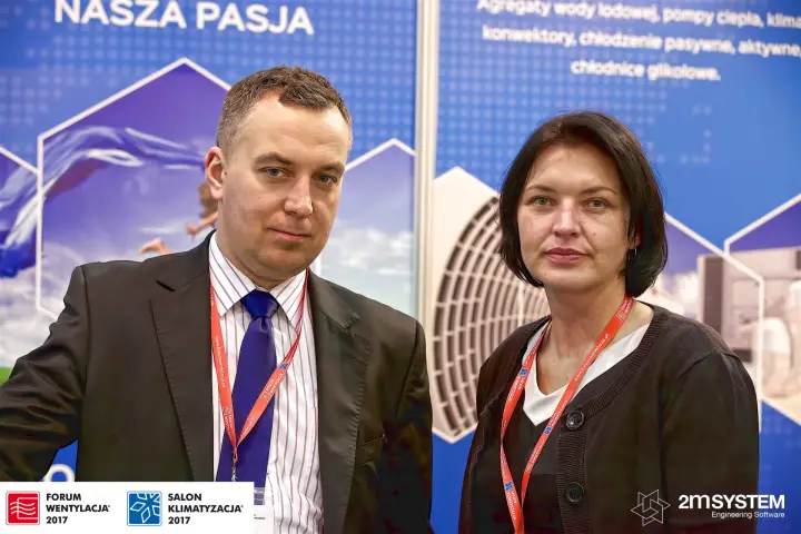 Two Hestor staff photographed in front of the blue stand graphics