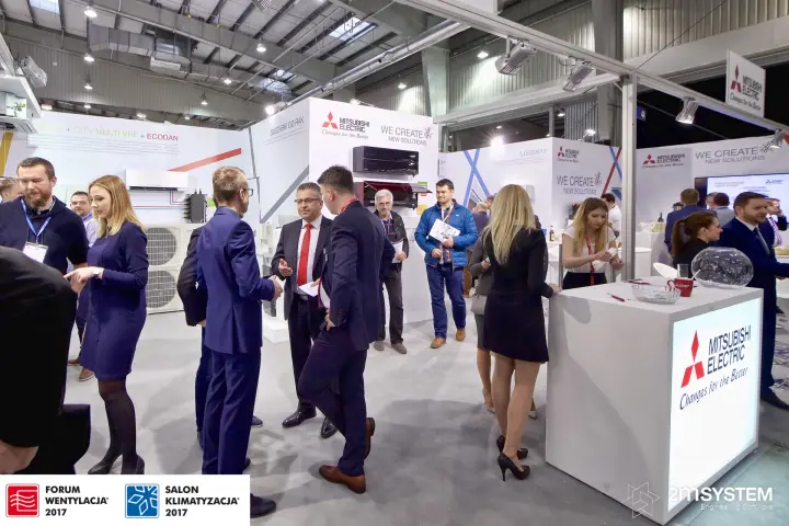 Visitors between the reception counter and display tower on Mitsubishi Electric stand