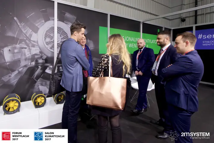 Visitors talk with Harmann staff beside yellow inline duct fans at Forum Wentylacja 2017
