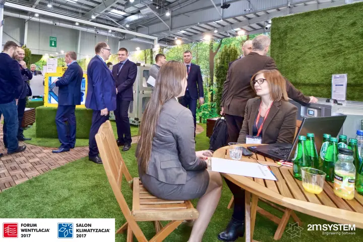 Visitors at wooden garden tables on the grass-covered VBW stand at Forum Wentylacja 2017