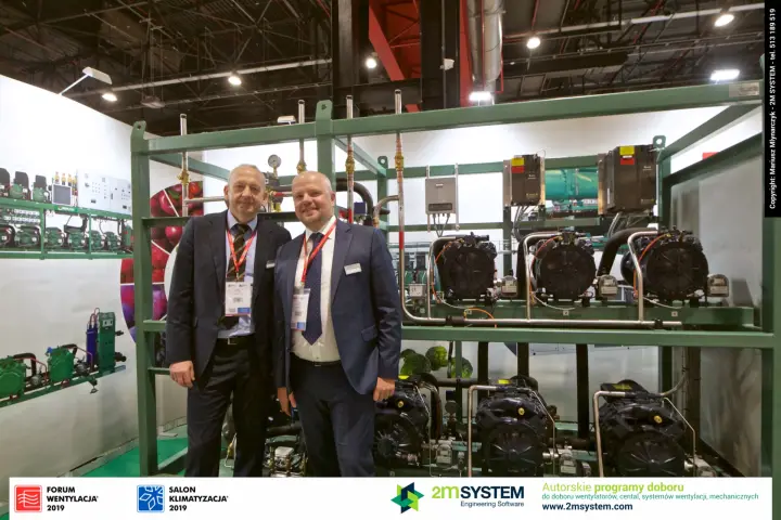 Two exhibitors in front of a green-framed Berling compressor rack