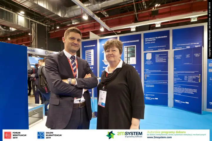 Two exhibitors pose in front of the Trox EK-JZ fire damper panels at Forum Wentylacja 2019