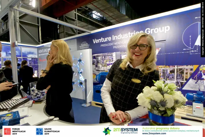 Venture Industries staff smiling at the counter by the projection wall at Forum Wentylacja 2019