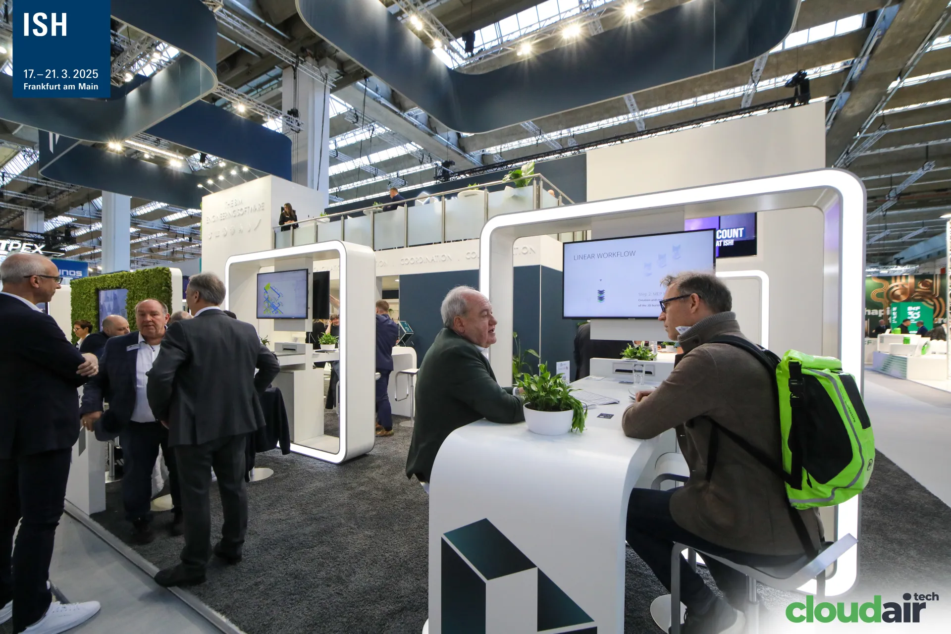 Linear meeting desks under illuminated white frames and an upper deck at ISH 2025