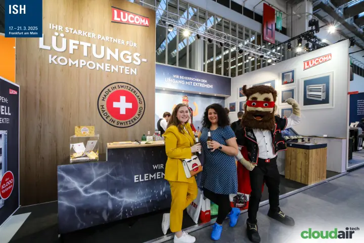Lucoma mascot flexes beside visitors at the Swiss-made stand at ISH 2025