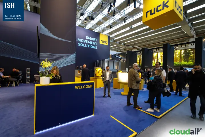 Ruck stand entrance with yellow-trimmed welcome counter and hanging logo cube at ISH 2025