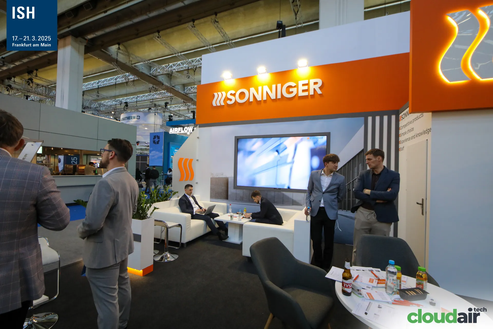 Sonniger lounge with white sofas and video screen under orange fascia at ISH 2025