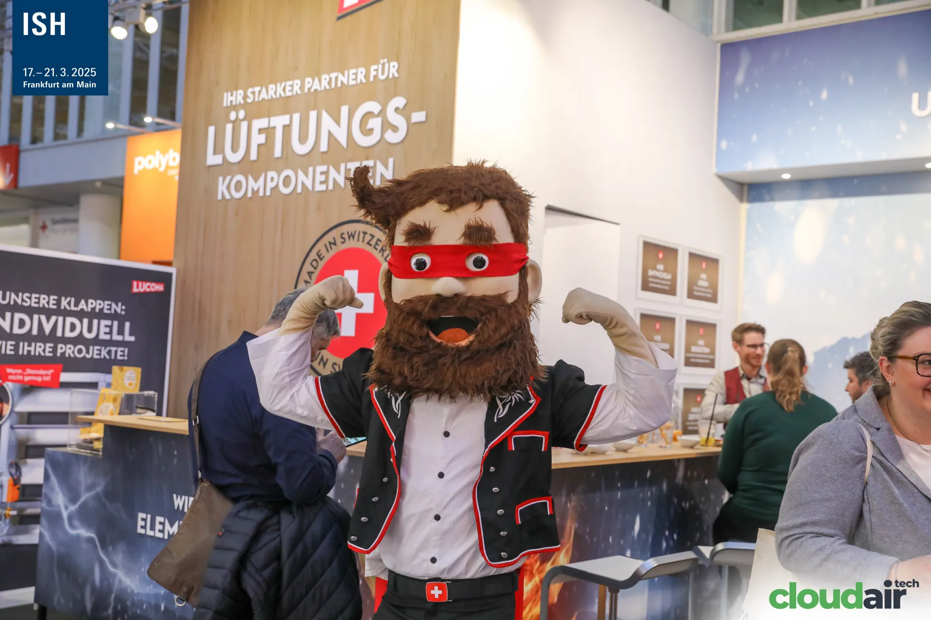 Swiss-themed mascot in front of the Lucoma ventilation components stand at ISH 2025