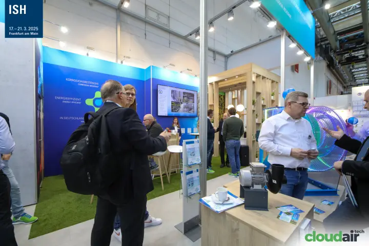 Visitors in conversation at the HLU stand near a small plastic fan at ISH 2025