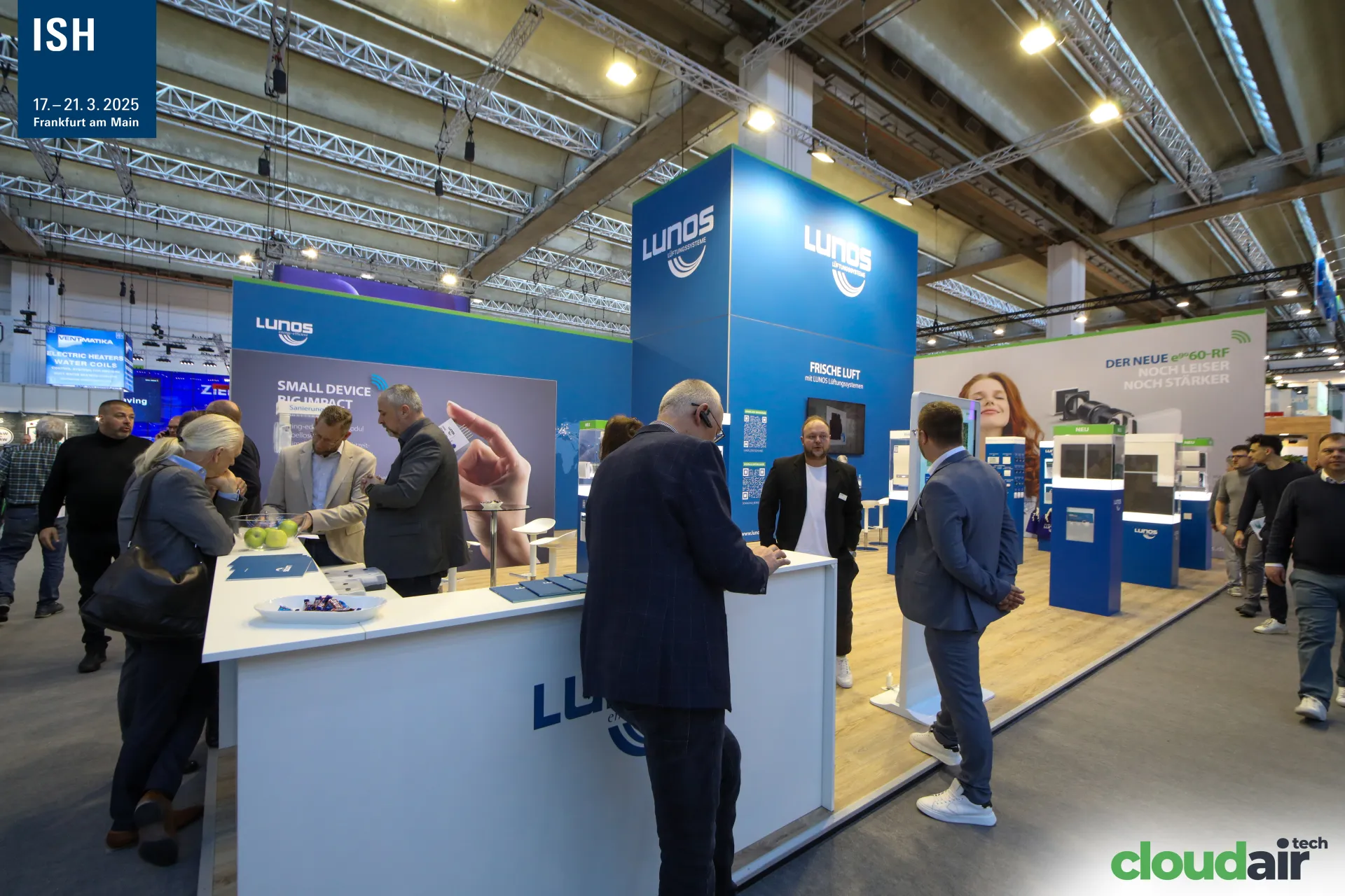 Visitors at the Lunos counter with "SMALL DEVICE BIG IMPACT" graphic at ISH 2025
