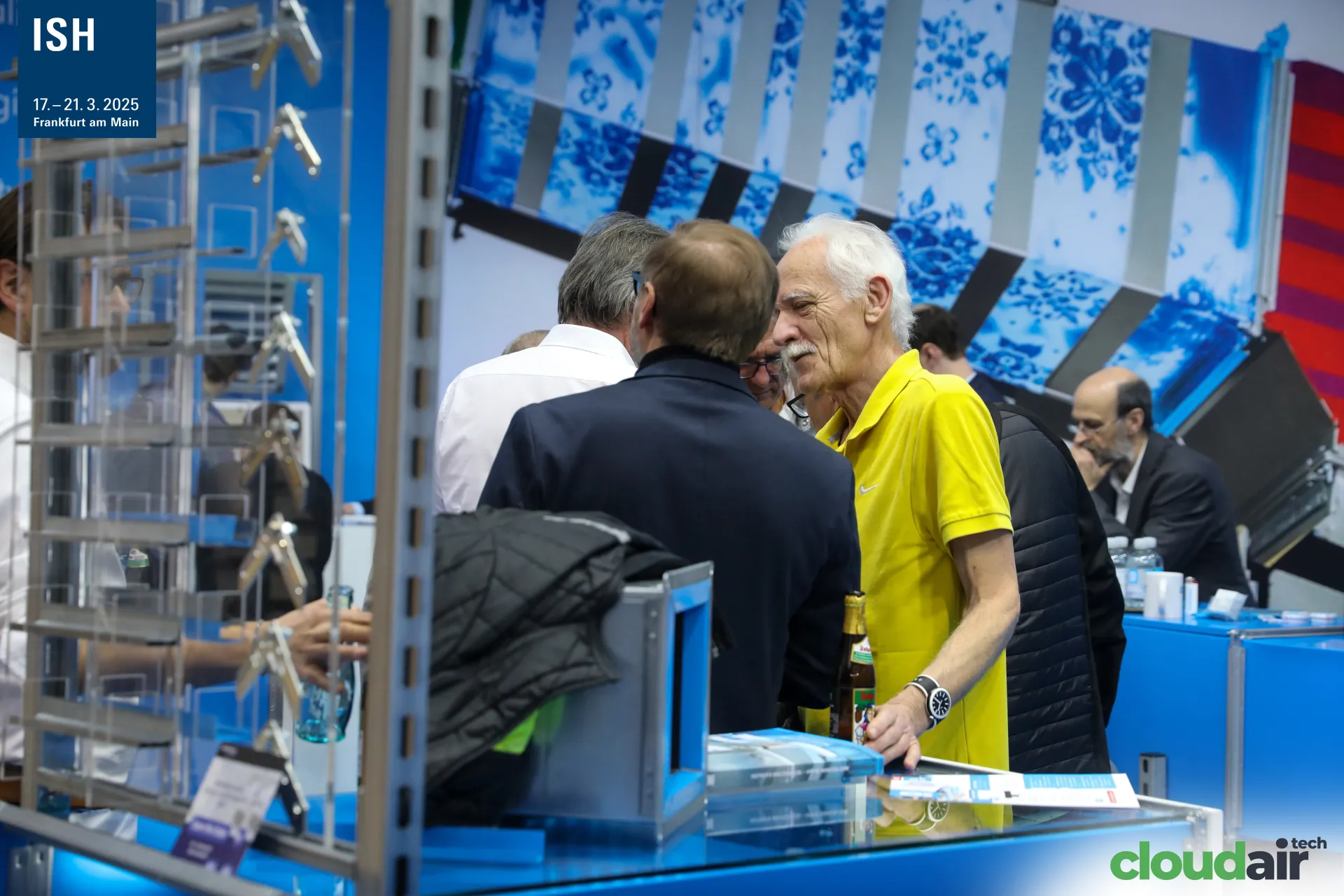 Visitors talking at the Airworker counter beside a display of duct parts at ISH 2025