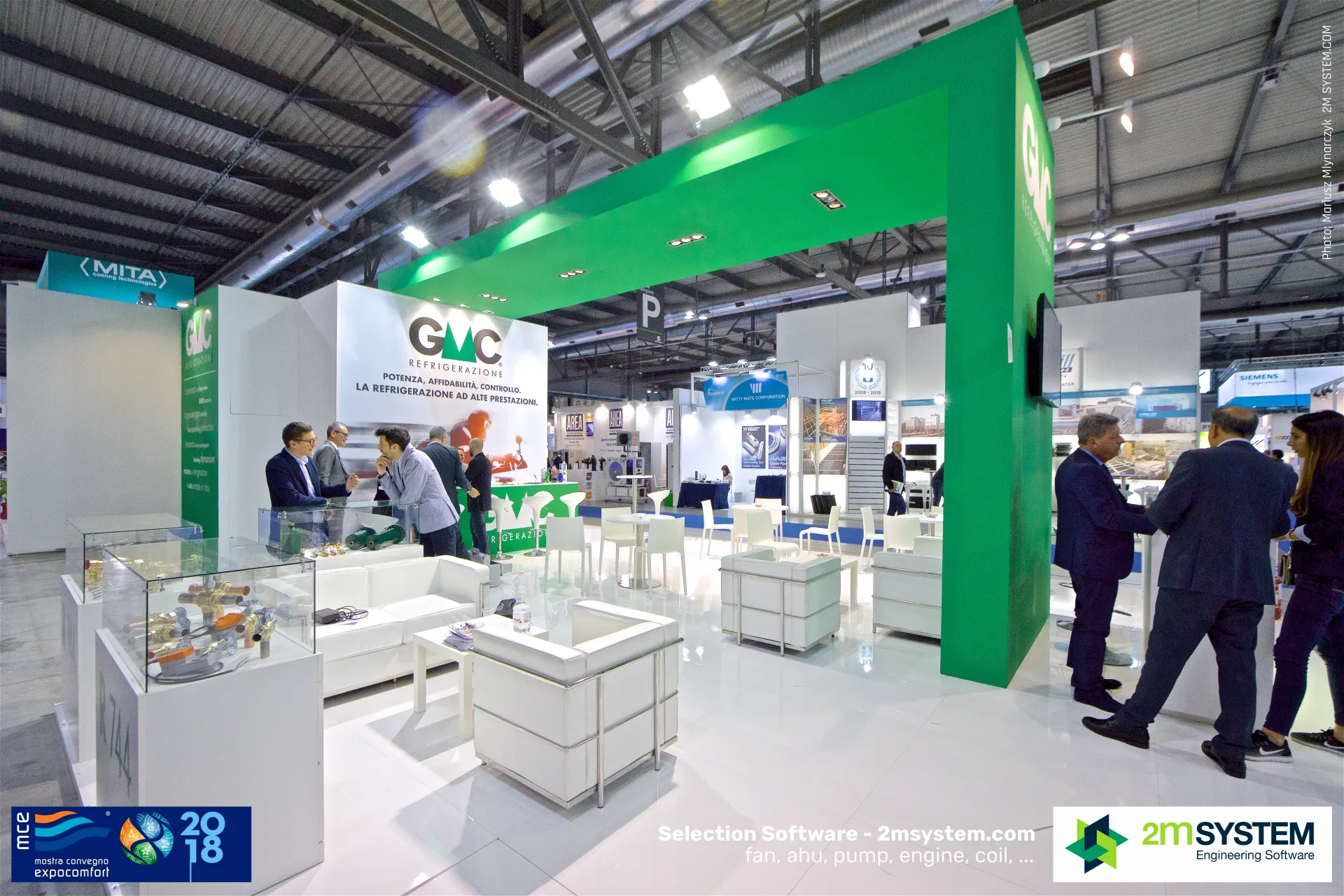 GMC stand overview with valve showcases and white lounge seating at MCE 2018