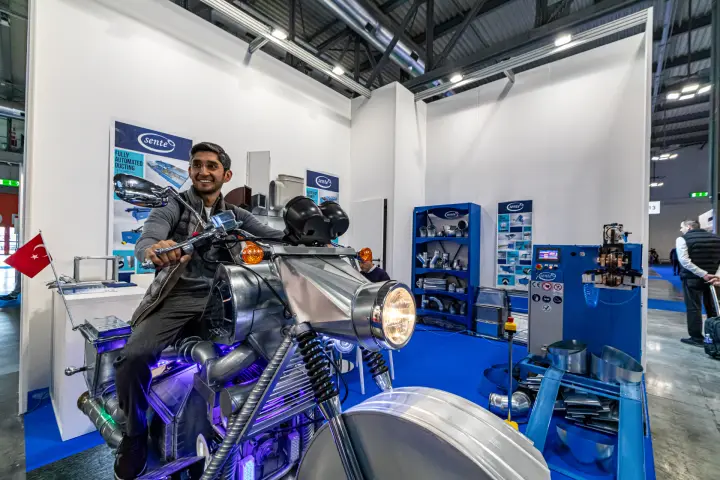 Duct-built motorcycle at Sente Makina with blue machine and fittings rack at MCE 2024