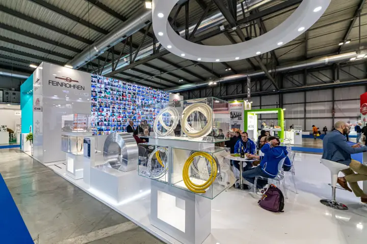 Feinrohren tube coils in glass cubes beside a wall of portrait photos at MCE 2024