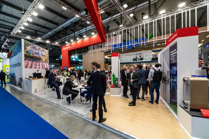 Red-framed stand with café seating and a heat exchanger display at MCE 2024