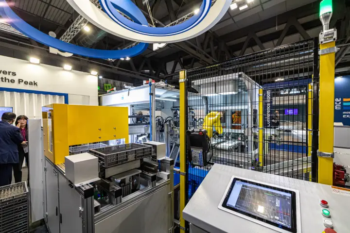Robotic production cell with yellow safety fence and touch control panel at MCE 2024