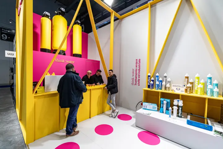 Think:water reception counter beneath yellow water treatment tanks on a magenta wall at MCE 2024