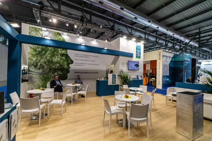 Trocellen lounge with round tables, reception counter and tree-face mural at MCE 2024