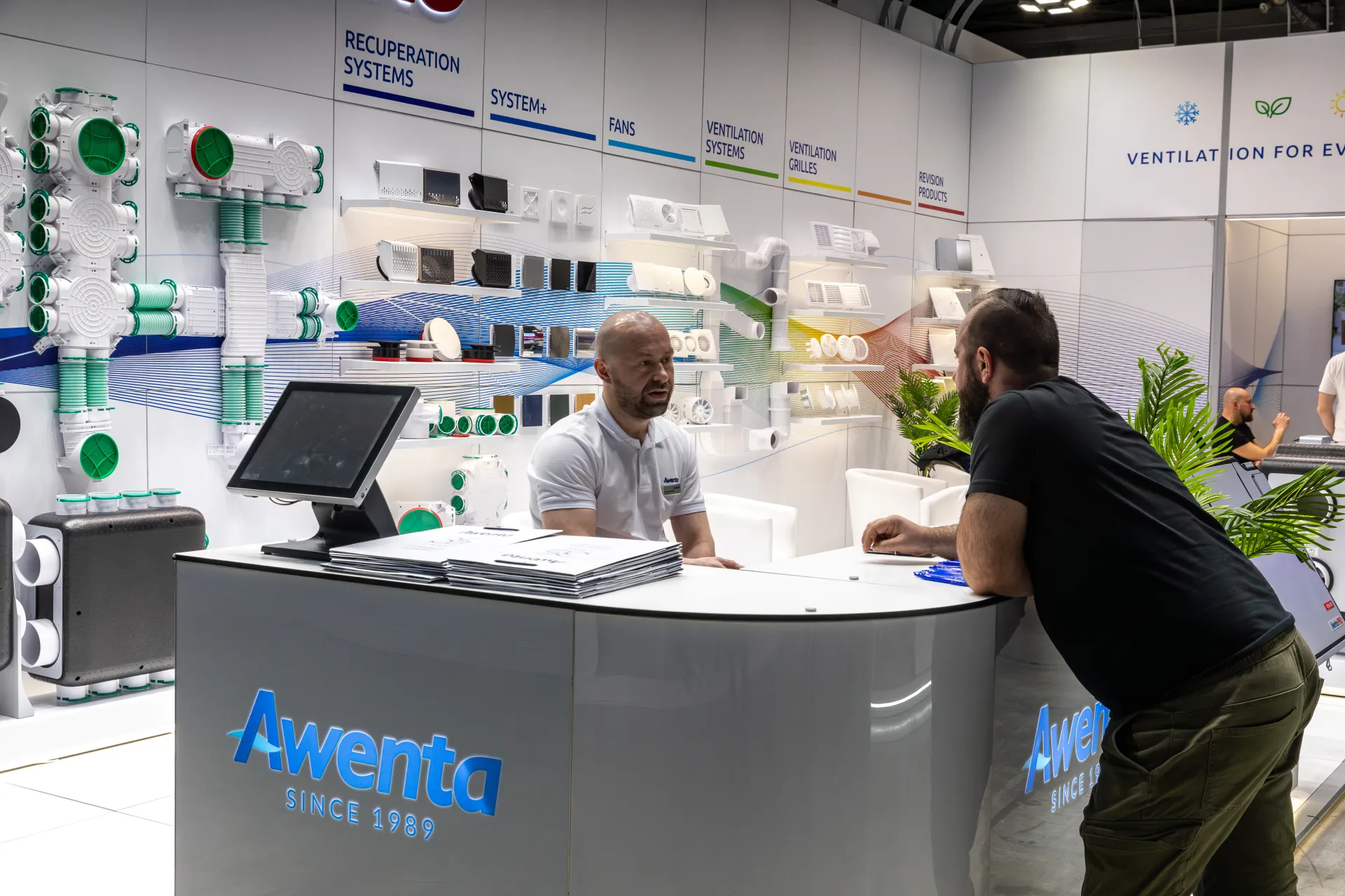 Awenta reception counter with blue SINCE 1989 logo and product wall at MCE 2026