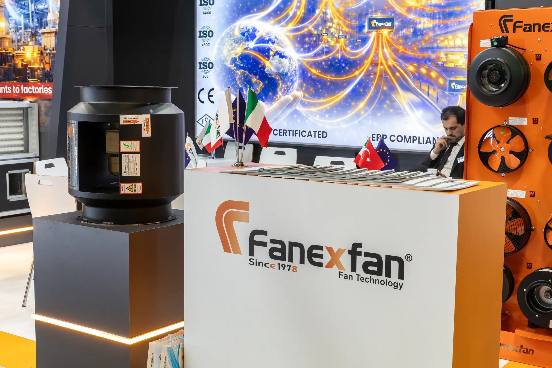 Fanexfan counter with flags, brochures and a black cylindrical fan at MCE 2026