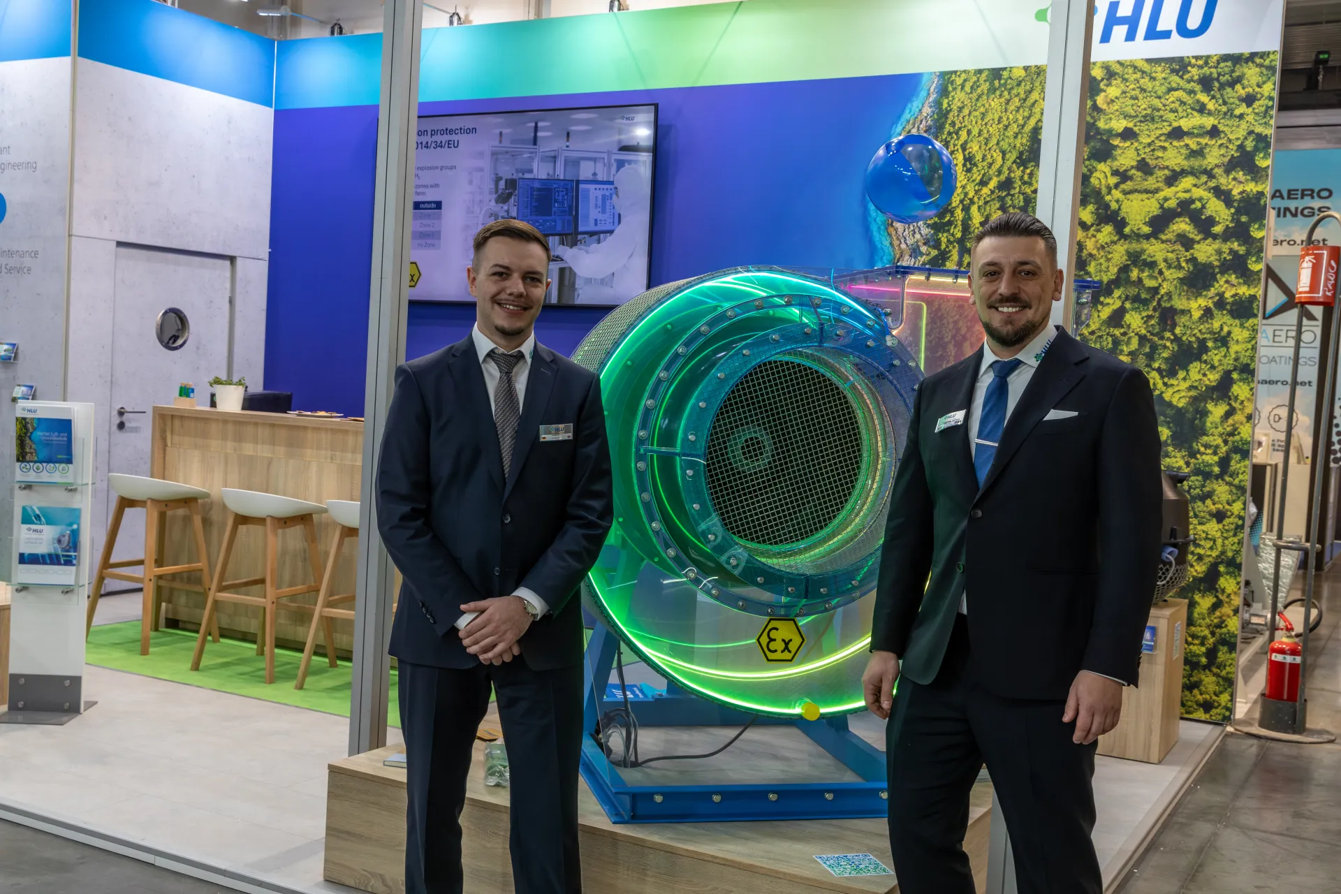 Green-lit transparent HLU fan model with brochure stand and bar area at MCE 2026