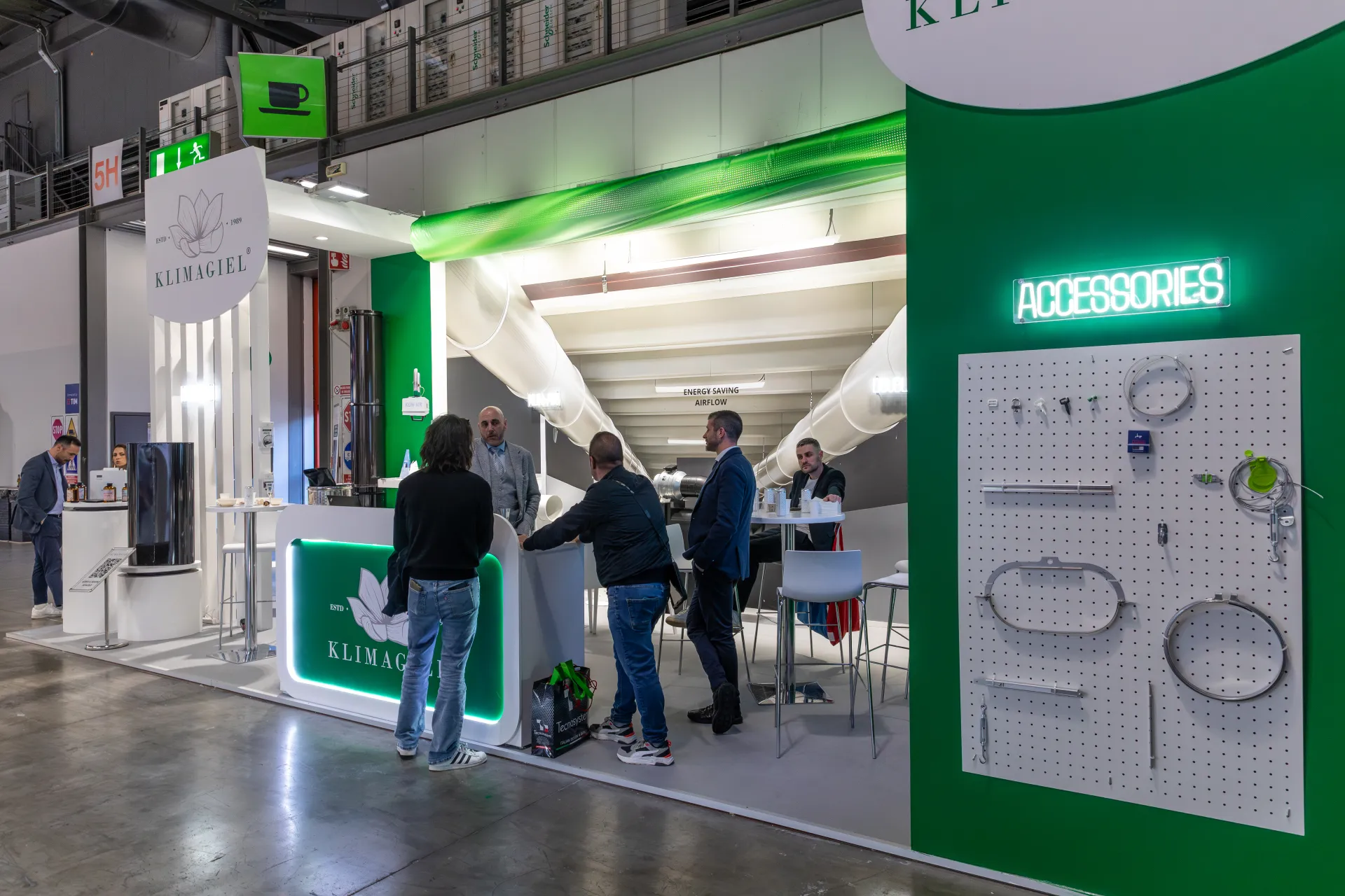 Klimagiel accessories pegboard with neon sign and overhead ducts at MCE 2026