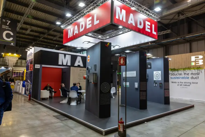 Madel stand C12 under a red banner on a lighting truss at MCE 2026