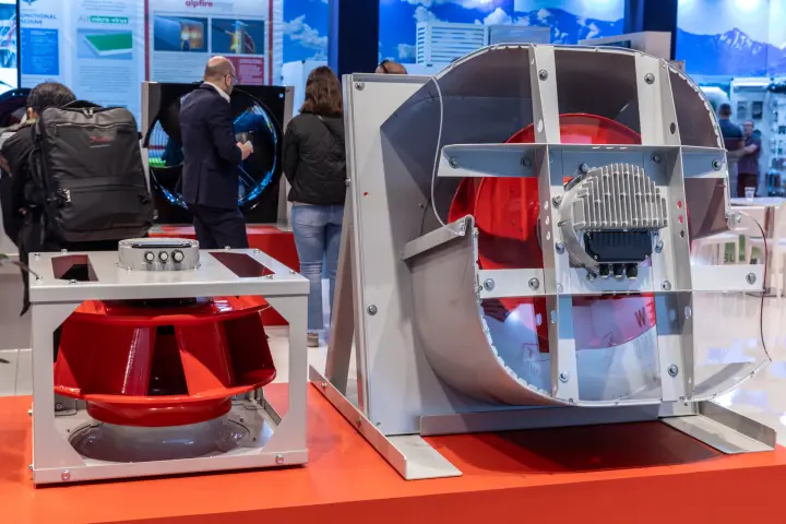 Plug fan with red impeller and a clear-sided scroll fan on an orange-red plinth at MCE 2026