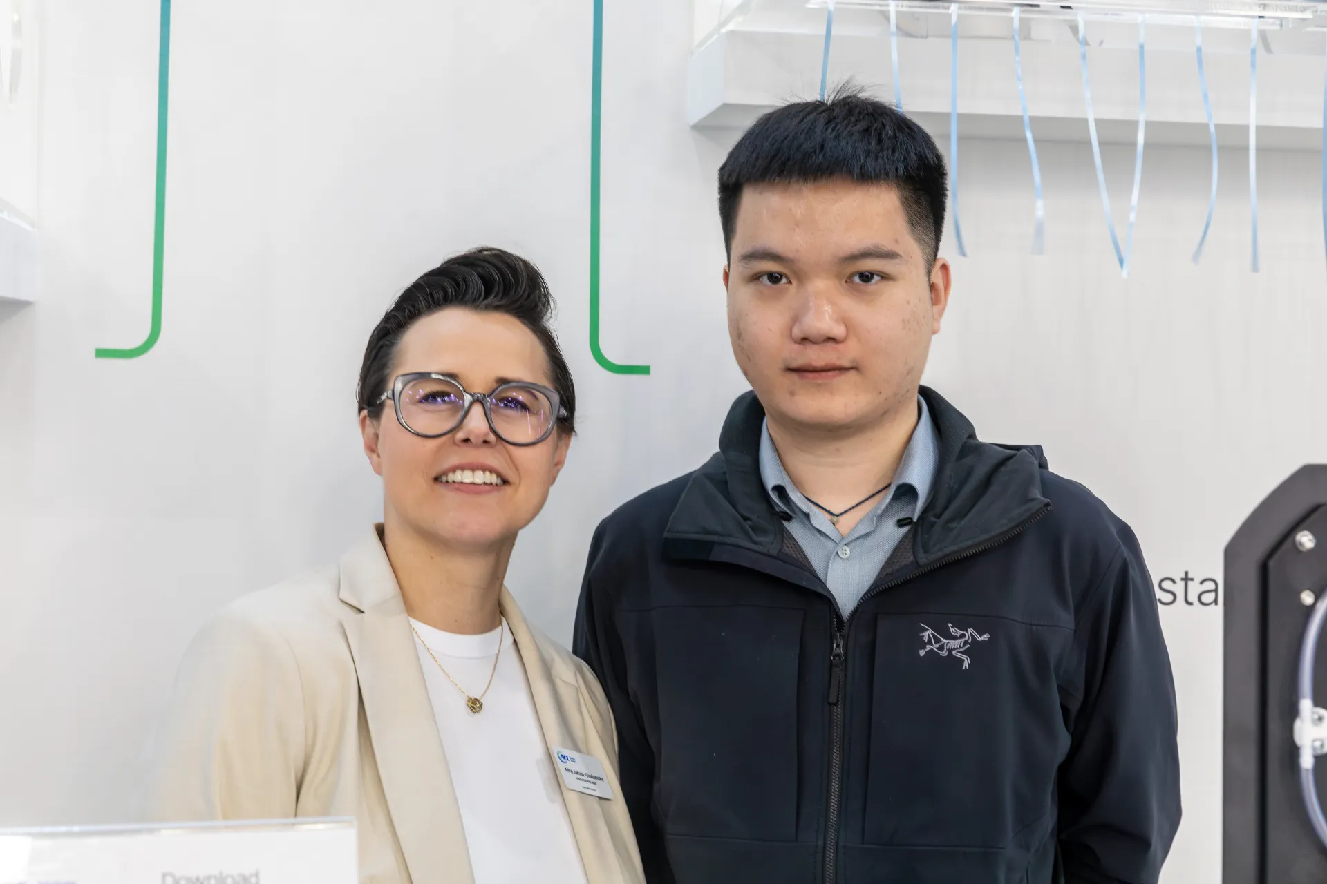 Portrait of two people at a white stand with acrylic shelf at MCE 2026