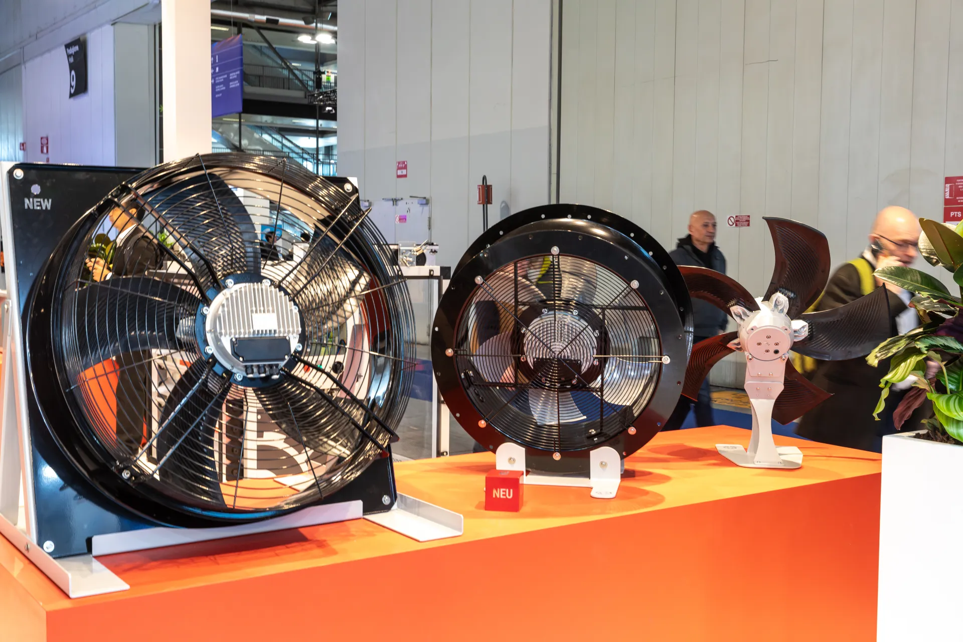 Two axial fans and an impeller with NEW and NEU tags on an orange plinth at MCE 2026