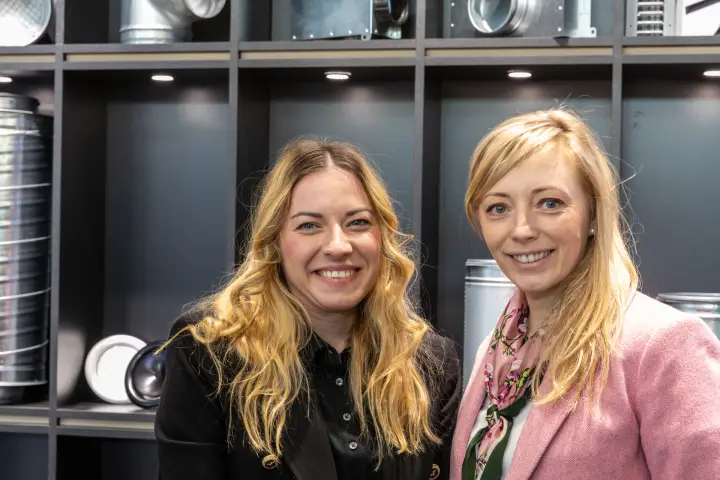 Two-person portrait in front of galvanised duct fittings shelving