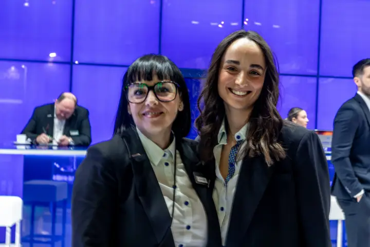 Two staff members posing in front of a blue glass wall
