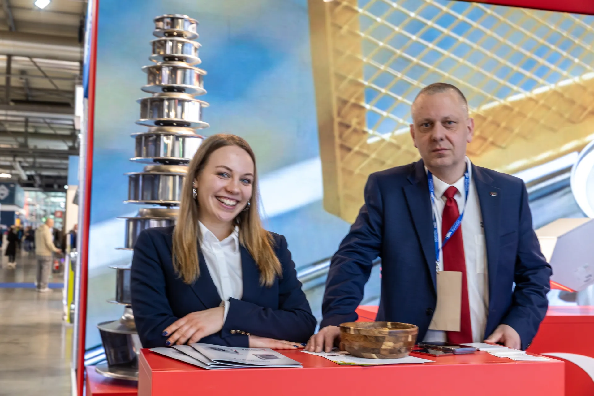 Two staff at a red counter beside the impeller tower, close portrait at MCE 2026