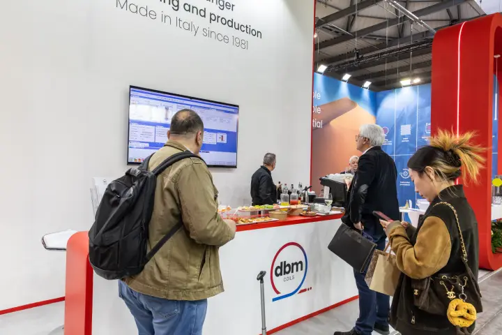 Visitors at the DBM Coils catering counter below a software screen at MCE 2026