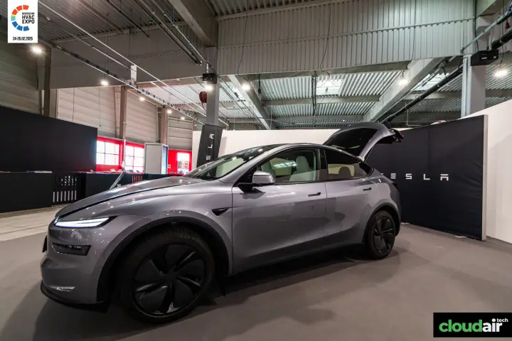 Grey Tesla electric car with open tailgate on a black-walled stand
